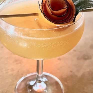 A fizzy Femme Brulee cocktail, focusing on its artistic apple garnish.